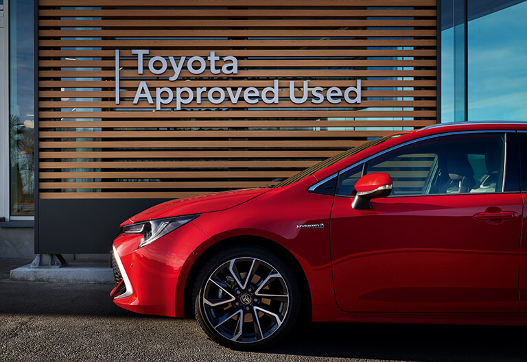 En röd Toyota framför en Toyota Approved Used-skylt